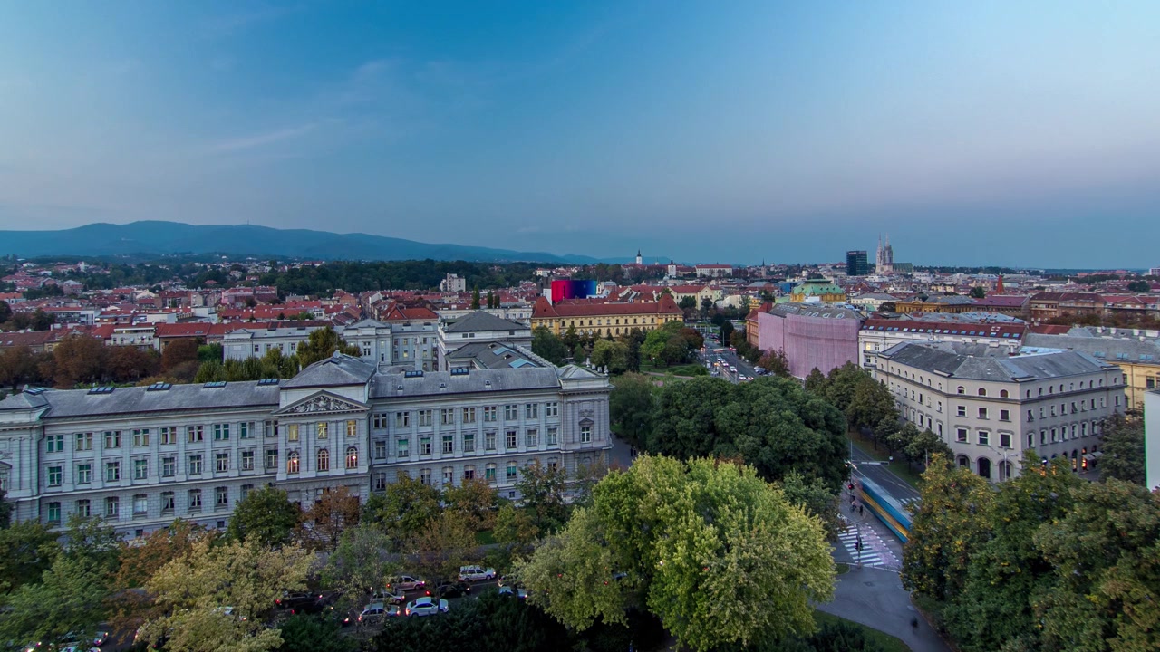 Panorama do centro da cidade em timelapse de transição do dia para a noite, filmado do topo de um arranha-céu com vista aérea para o cruzamento em frente ao teatro nacional e museu em Zagreb, Croácia, após o pôr do sol.