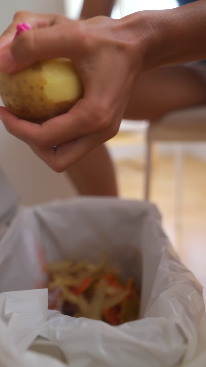 Hands peeling a potato over a trash can