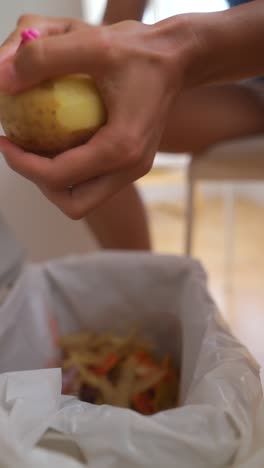 hands peeling a potato over a trash can