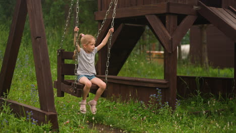 little child plays swings with chains on ground on lawn