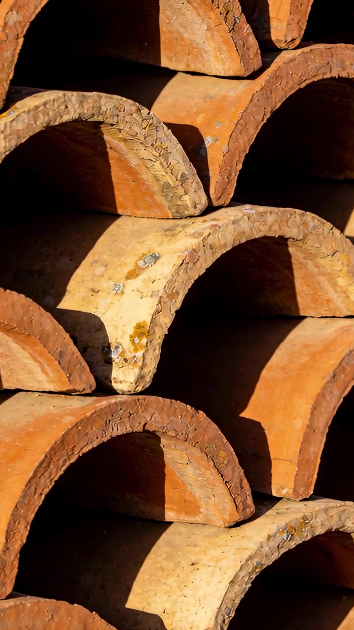 Video verticale: Telecamera che si sposta rivelando tegole di terracotta impilate all'aperto, documentando una tegola chiara.