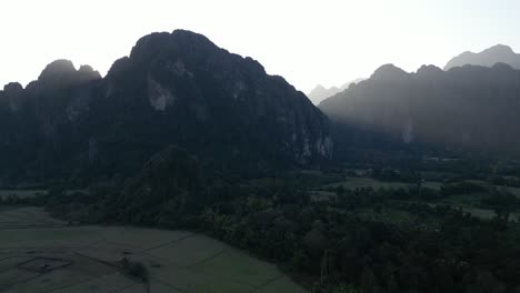 drone shot of sun rising behind mountains in vang vieng, the adventure capital of laos