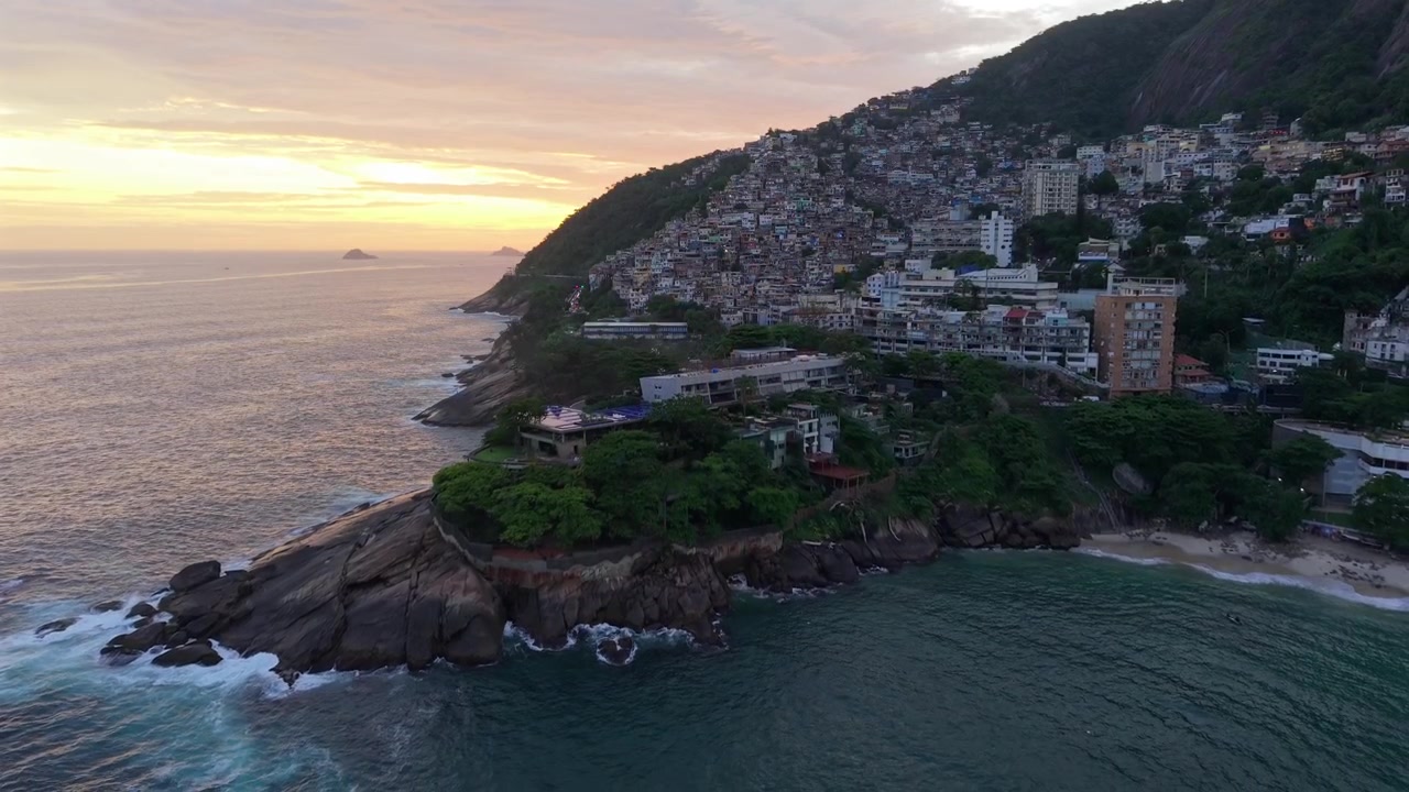Filmagem suave de drone afastando-se da vibrante favela do Vidigal em direção ao oceano ao pôr do sol