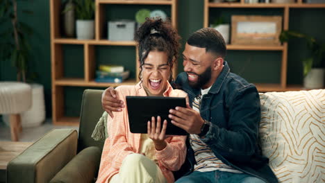 couple laughing together while using a tablet on the couch