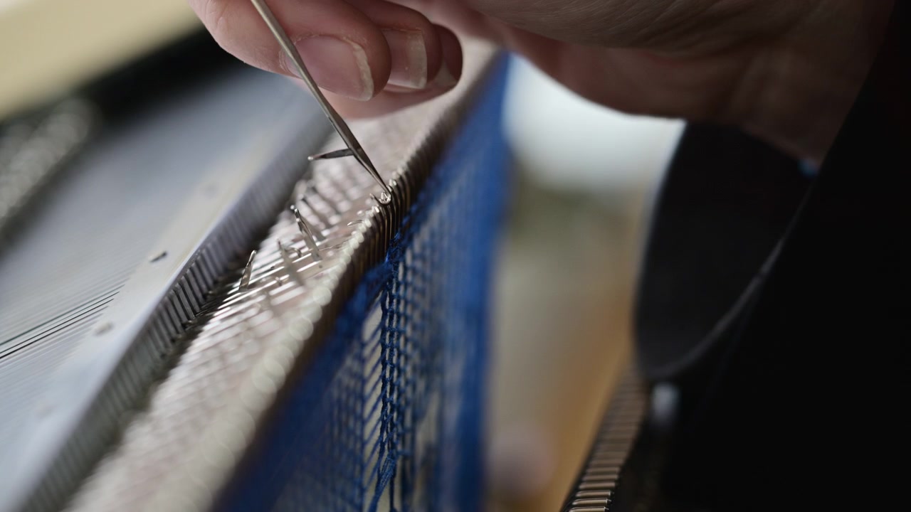 Nahaufnahme einer Frau, die blauen Strickstoff an einer Flachstrickmaschine anpasst.
