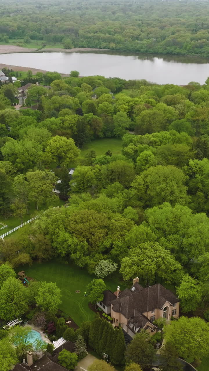 Nice private houses half-hidden in the green trees. Beautiful rural American suburb located at the river bank. top view. Vertical video