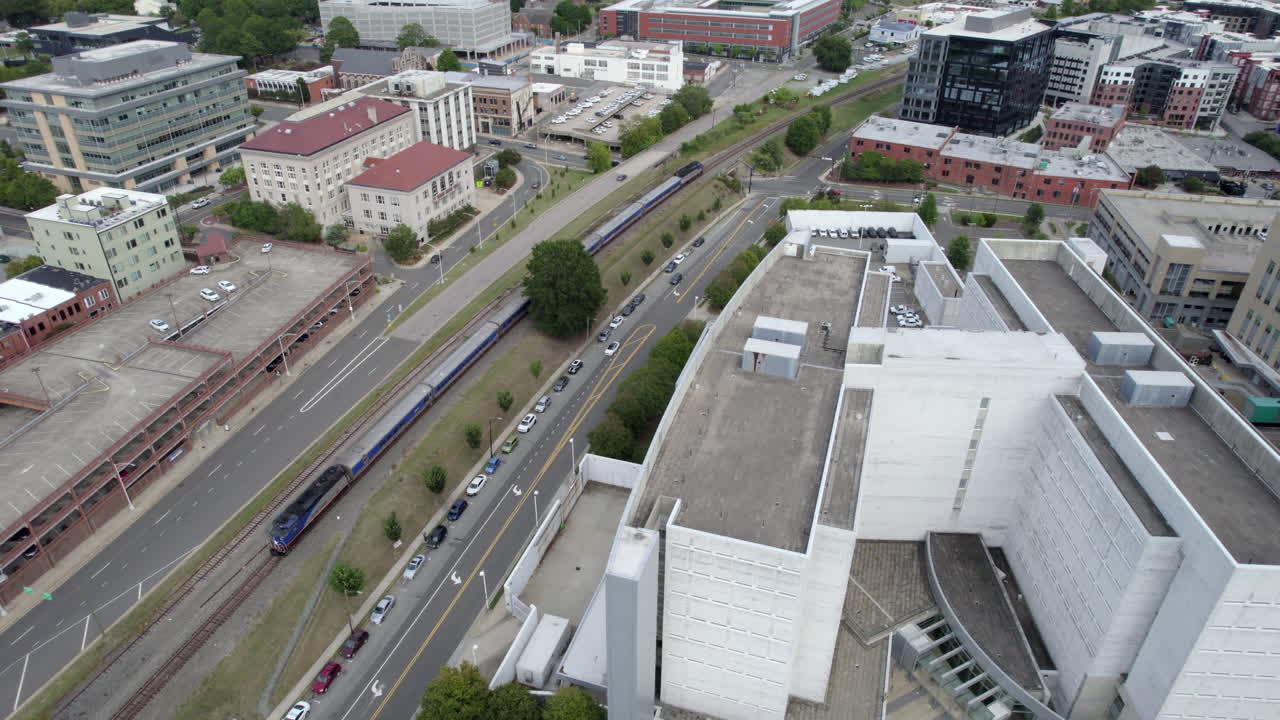 Aerial drone follows train as it rolls out of train station, depot. Urban. Commuter rail.