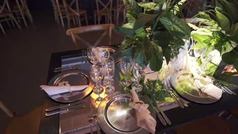 Elegante-Mesa-De-Boda-Con-Cristalería,-Vegetación-E-Iluminación-Suave-Para-Una-Velada-Romántica