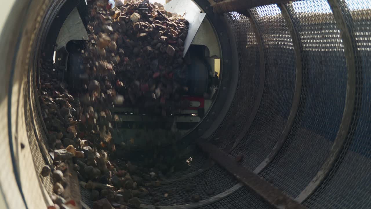 Stones Mechanical Screening - gravel with soil and sand falls from the belt conveyor to spinning cylindrical sifter with holes sifting of soil, crushed stone and other loose building materials