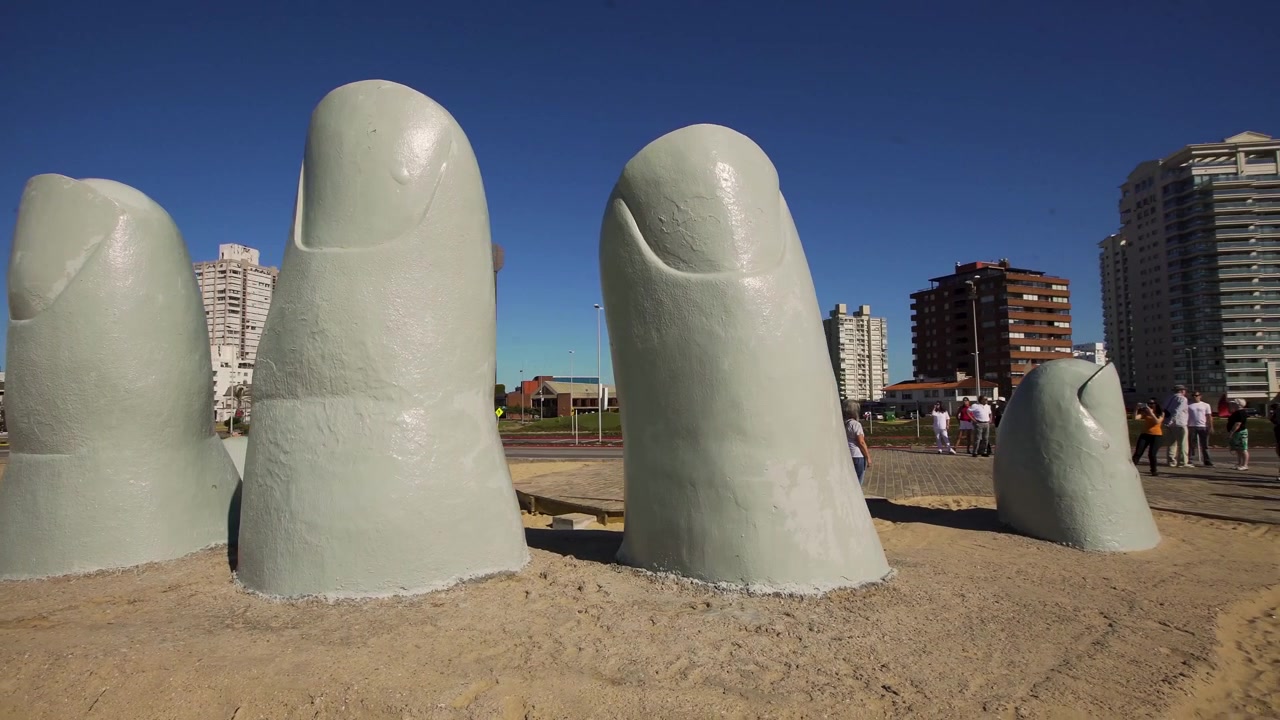 Riprese orbitali della statua La Mano a Punta del Este con sfondo urbano. Uruguay