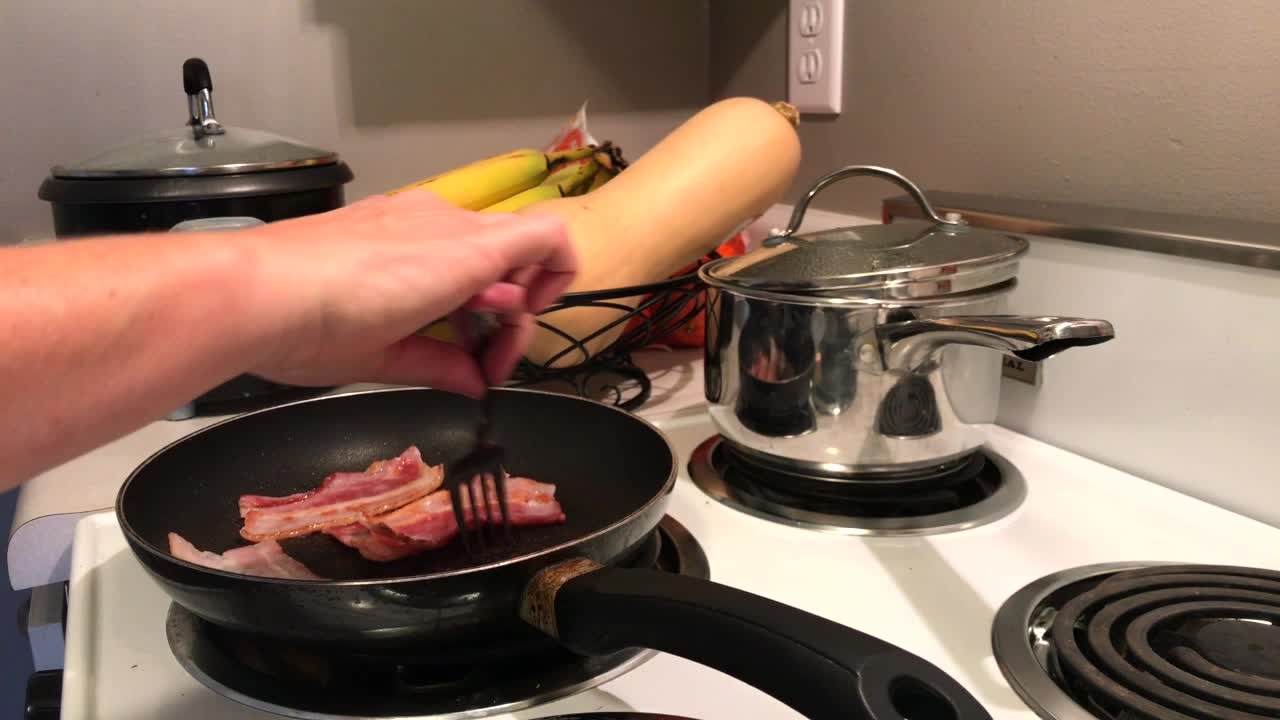 카우카시안 여성의 손은 포크로 베이컨을 기고 있습니다.