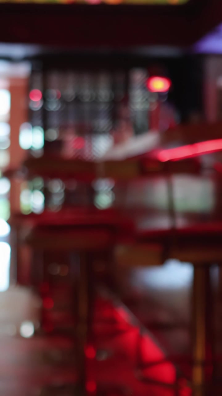 En person forlader en moderne bar eller restaurant med rød accentbelysning, gående mod et lyst ydre, mens kameraet forbliver stationært, og fokus blødgøres.