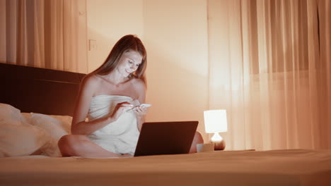mujer relajándose en la cama por la noche usando portátil y teléfono