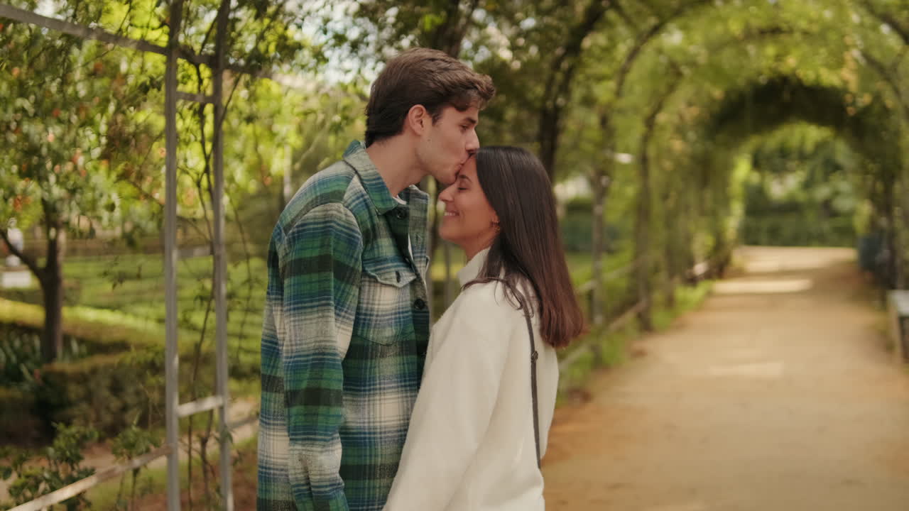 Happy young partners man and woman standing holding hands against green arch