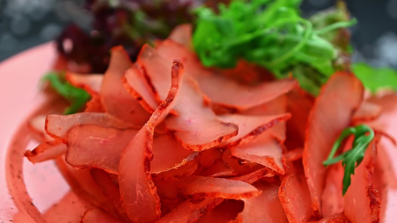 Fette di carne disposte su un piatto con lattuga e guarnizione in una cucina. Fette di carne rossa sono disposte con cura su un piatto rosa accanto a verdure fresche