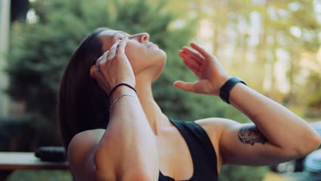 a young woman in a black tank top puts her hair up in a ponytail after her golden hour run and yoga workout