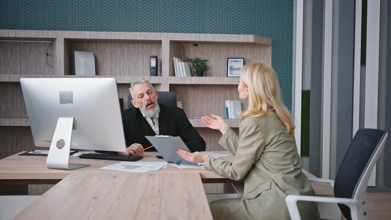 Commercialista donna matura che si reca nell'ufficio del CEO uomo e inizia a discutere il piano finanziario aziendale, mostrando il budget