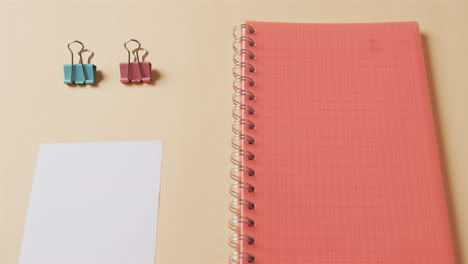 close up of red notebook and school stationery arranged on beige background, in slow motion