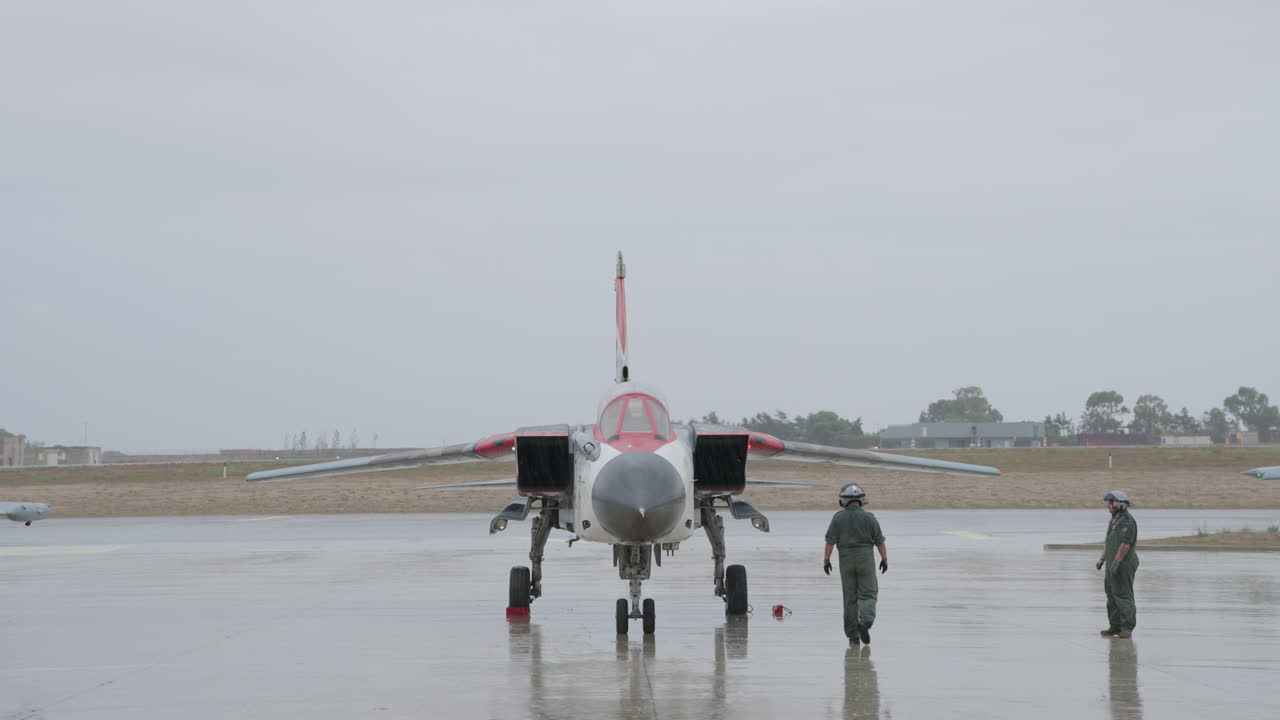 Piloti militari ispezionano un jet da combattimento su una pista bagnata