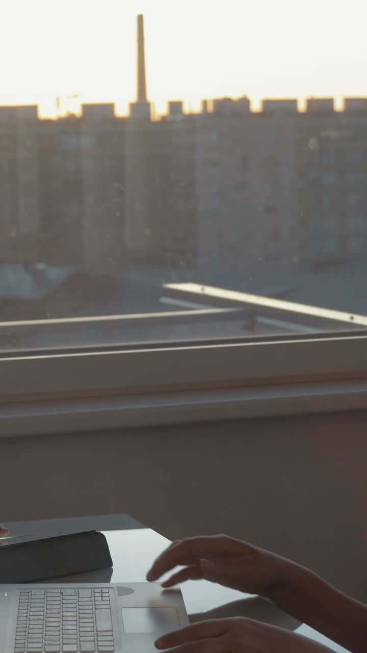 Pessoas trabalhando em um laptop perto de uma janela ao pôr do sol