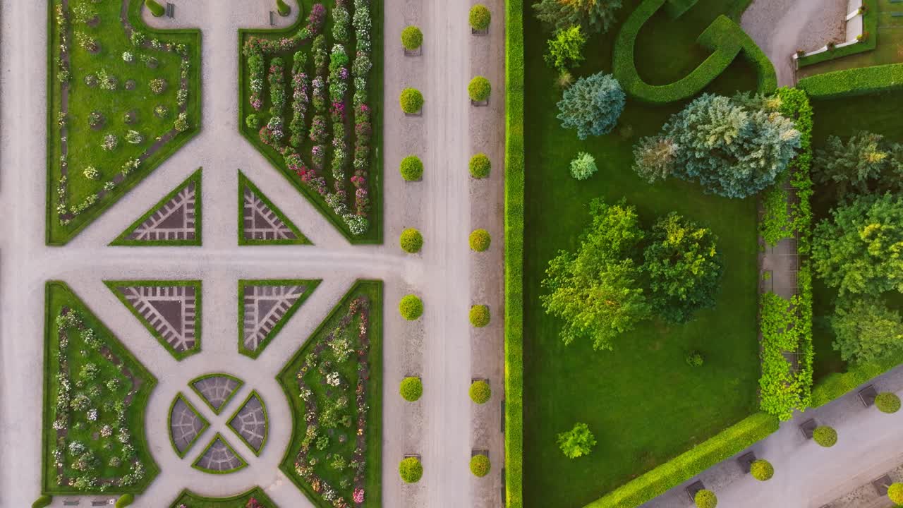 Drone slowly flies forward above ornate flower beds and clipped hedges at dawn
