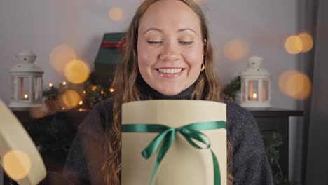 european woman looks inside round gift box at joyful holiday christmas season, yellow light bokeh flutters