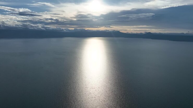 Tramonto che si riflette sul Lago Toba con nuvole e montagne distanti, atmosfera serena