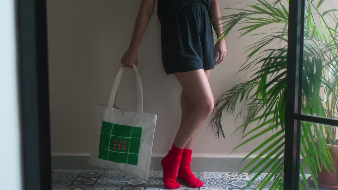 Mujer presentando una bolsa tote ecológica personalizada con diseño verde y rojo, mostrando moda moderna y opciones de estilo de vida consciente para la vida urbana