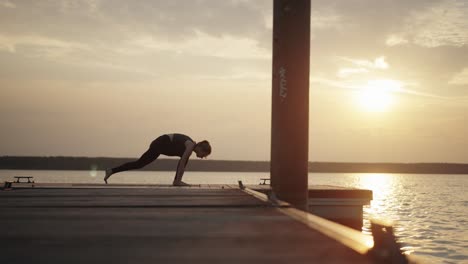 young woman doing dynamic yoga flow on jetty at sunset, slow motion