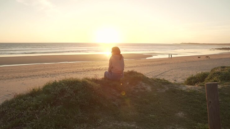 Mulher viajante sentada em uma colina com o céu do pôr do sol perto do mar