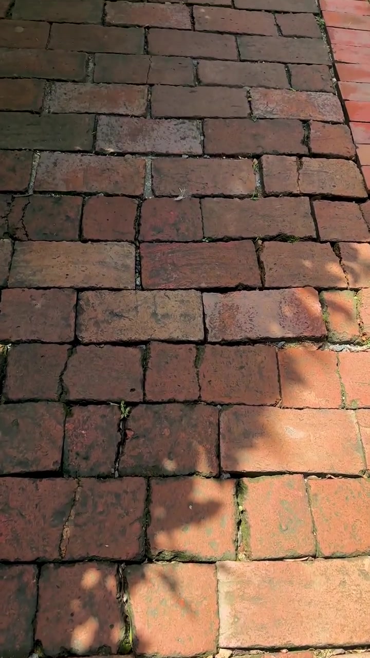 First-person perspective tracking shot walking over ancient weathered red brick pathway under dappled sunlight.