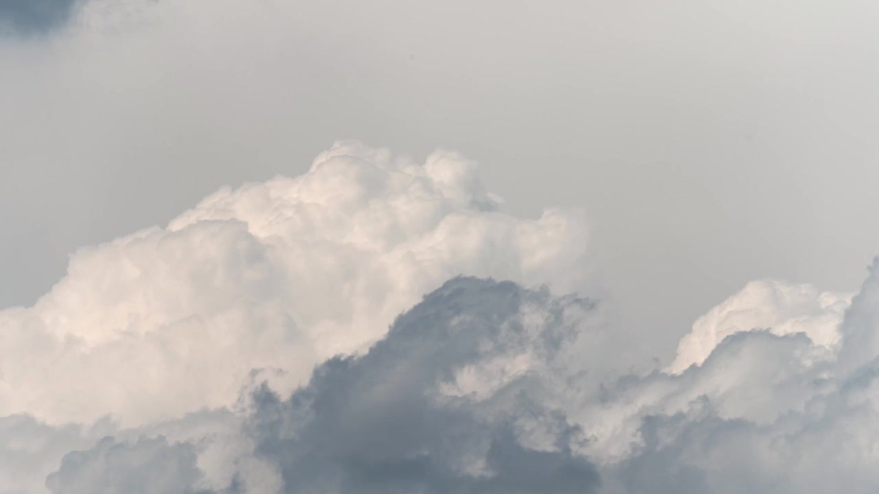 Time lapse of towering cumulus clouds illuminated by soft natural light against a pale sky.