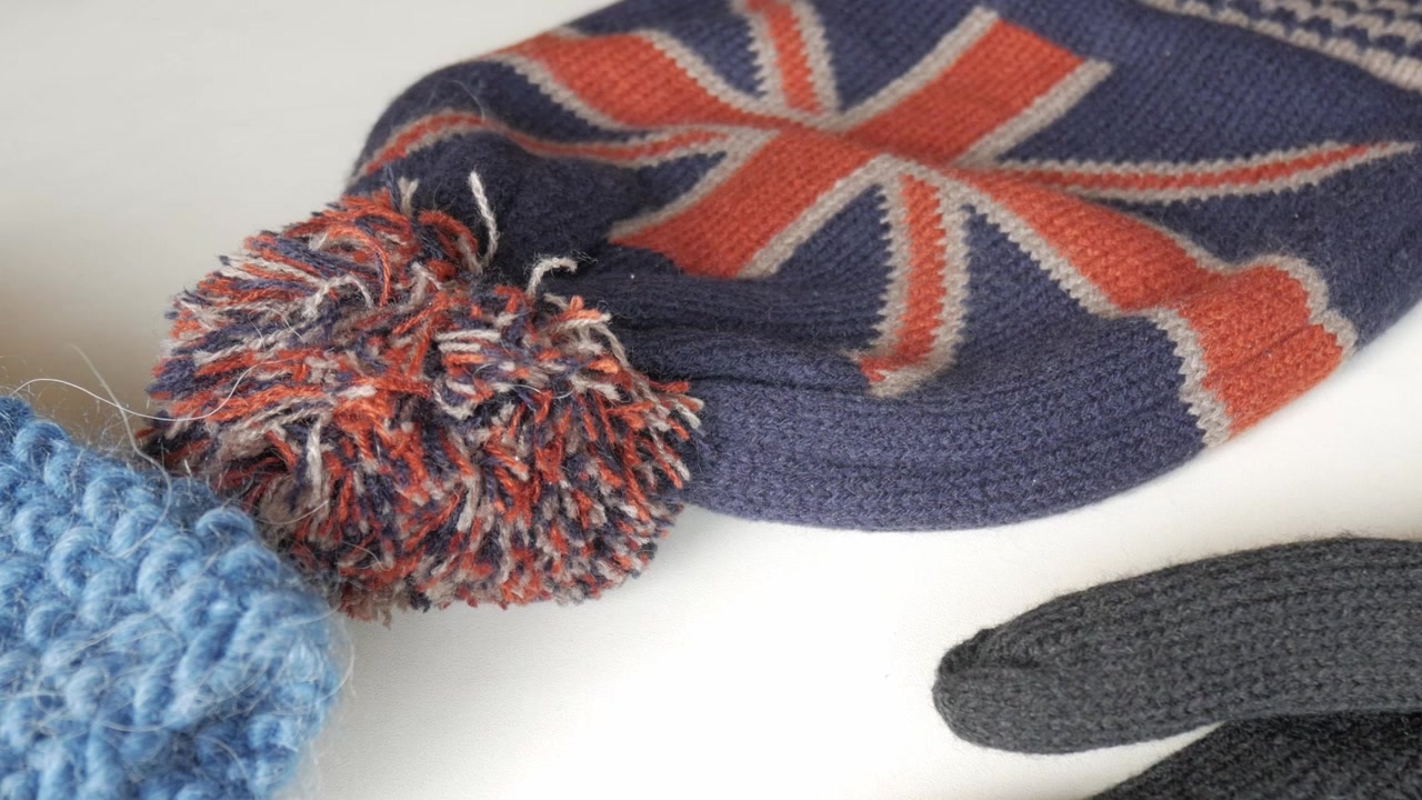 Gorro de inverno de malha colorido com pompom e design da Union Jack em uma superfície branca.