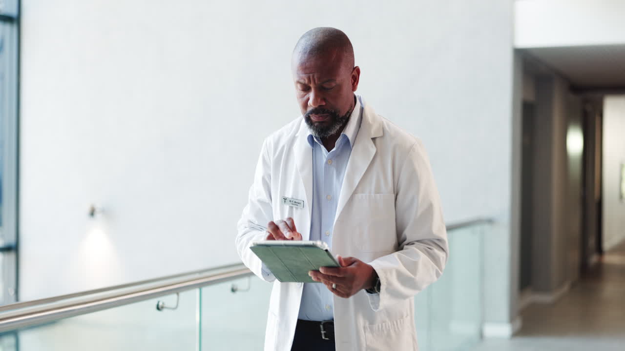 Male Doctor Walking and Using Digital Tablet in Hospital Corridor