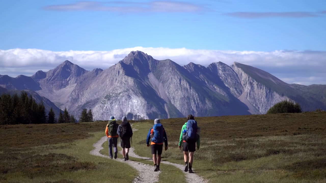 Escursionisti su sentiero di montagna in avvicinamento alle vette, piccolo gruppo con zaini lungo un sentiero sterrato serpeggiante.
