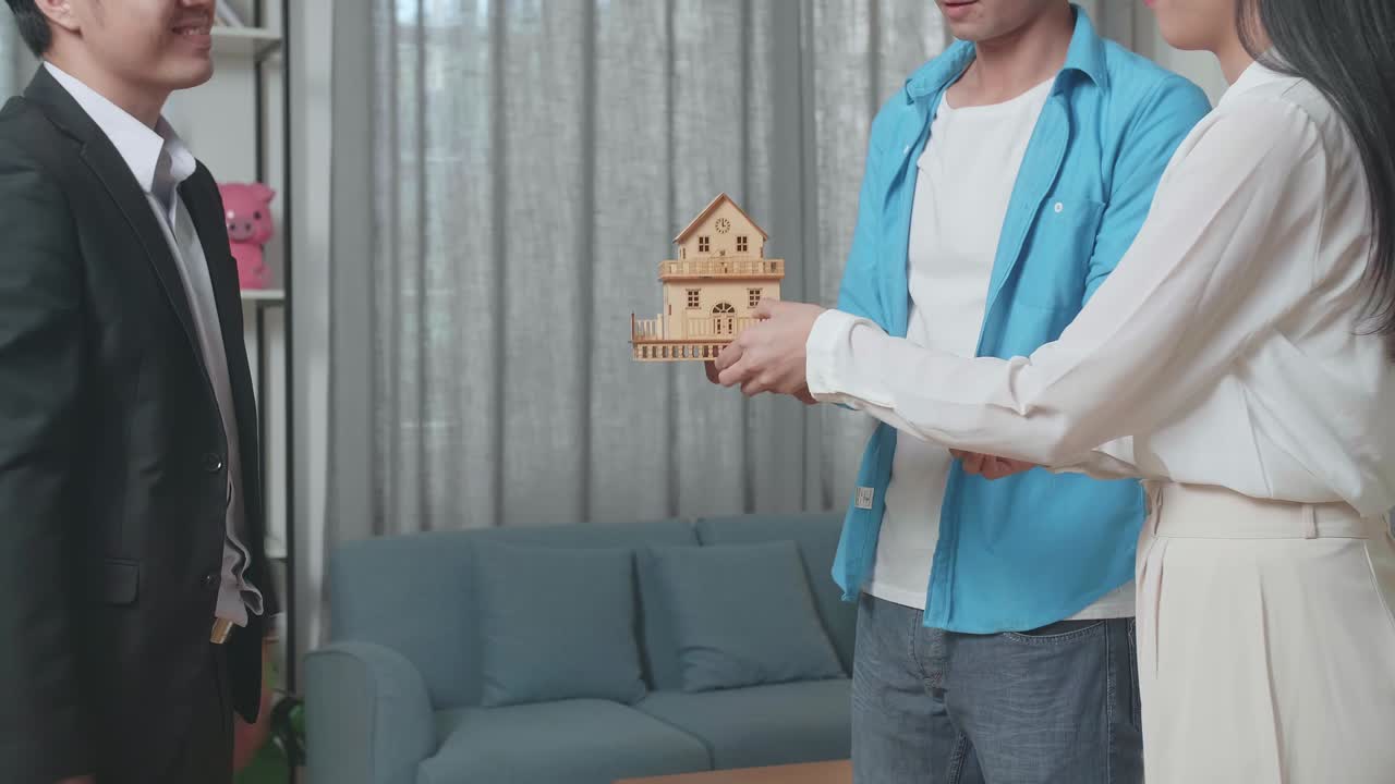 아시아 부동산 대리인이 팔기 위해 집에 엄지손가락을 올리기 전에 부부에게 집 모델을 제공합니다.
