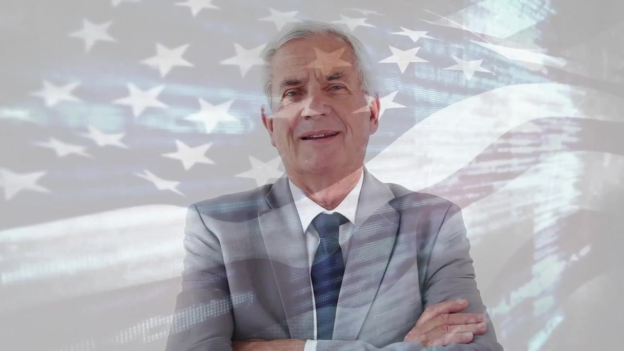 Hombre mayor centrado, después de una pausa, cruzando los brazos y sonriendo, mientras una superposición de bandera se desplaza, señalando política.
