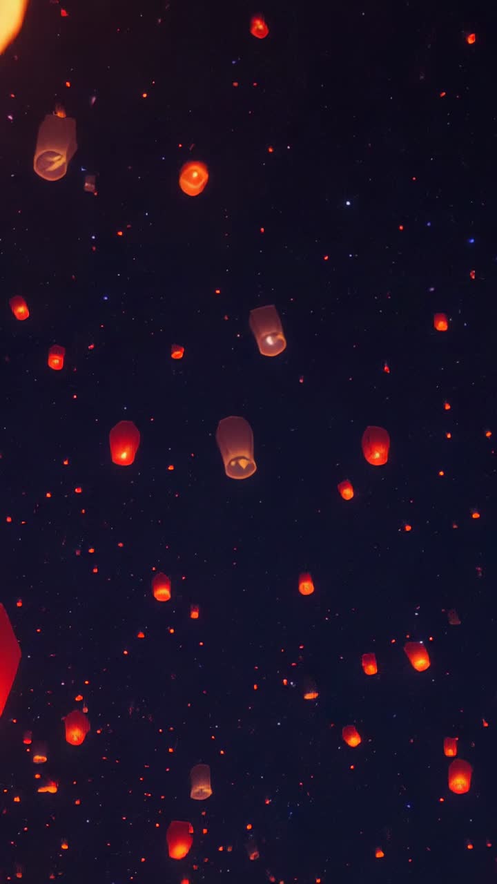 Vertical video: Cluster of glowing paper lanterns drifting upward in night sky, after release