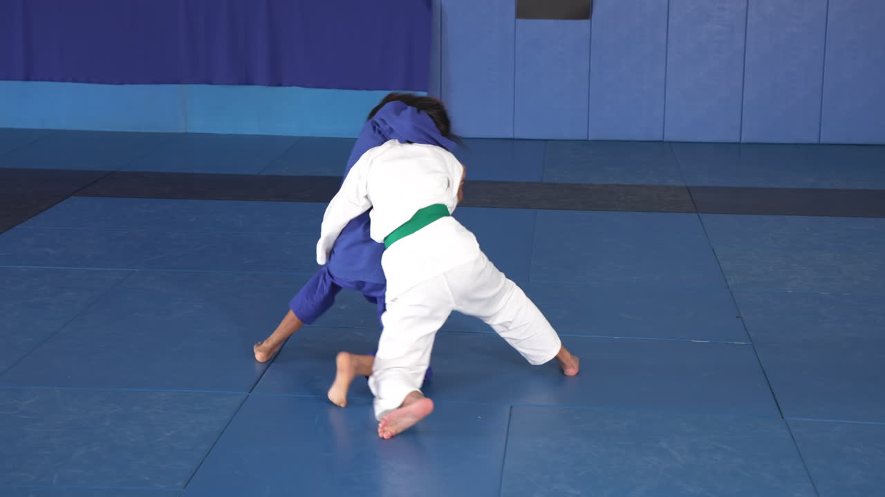 Practicing judo, two athletes in blue uniforms grappling on mat