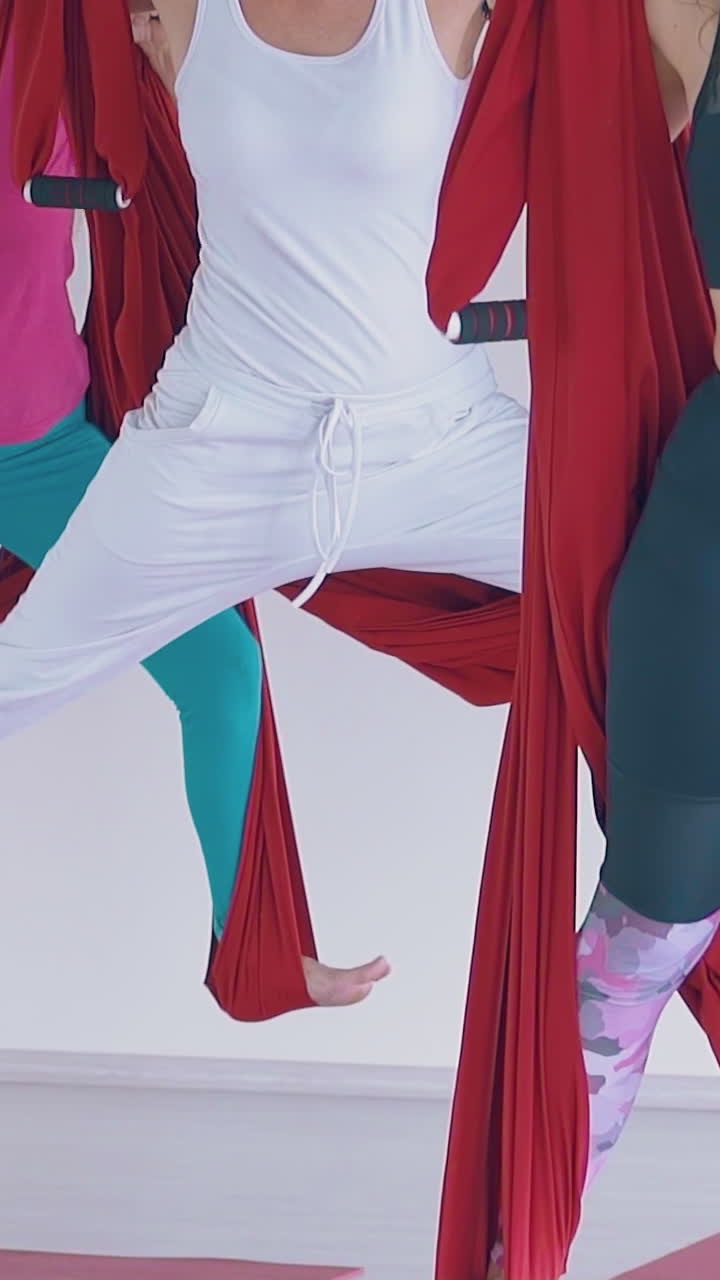 concentrated ladies stretch legs standing and holding long oriental fly yoga hammocks close view slow motion