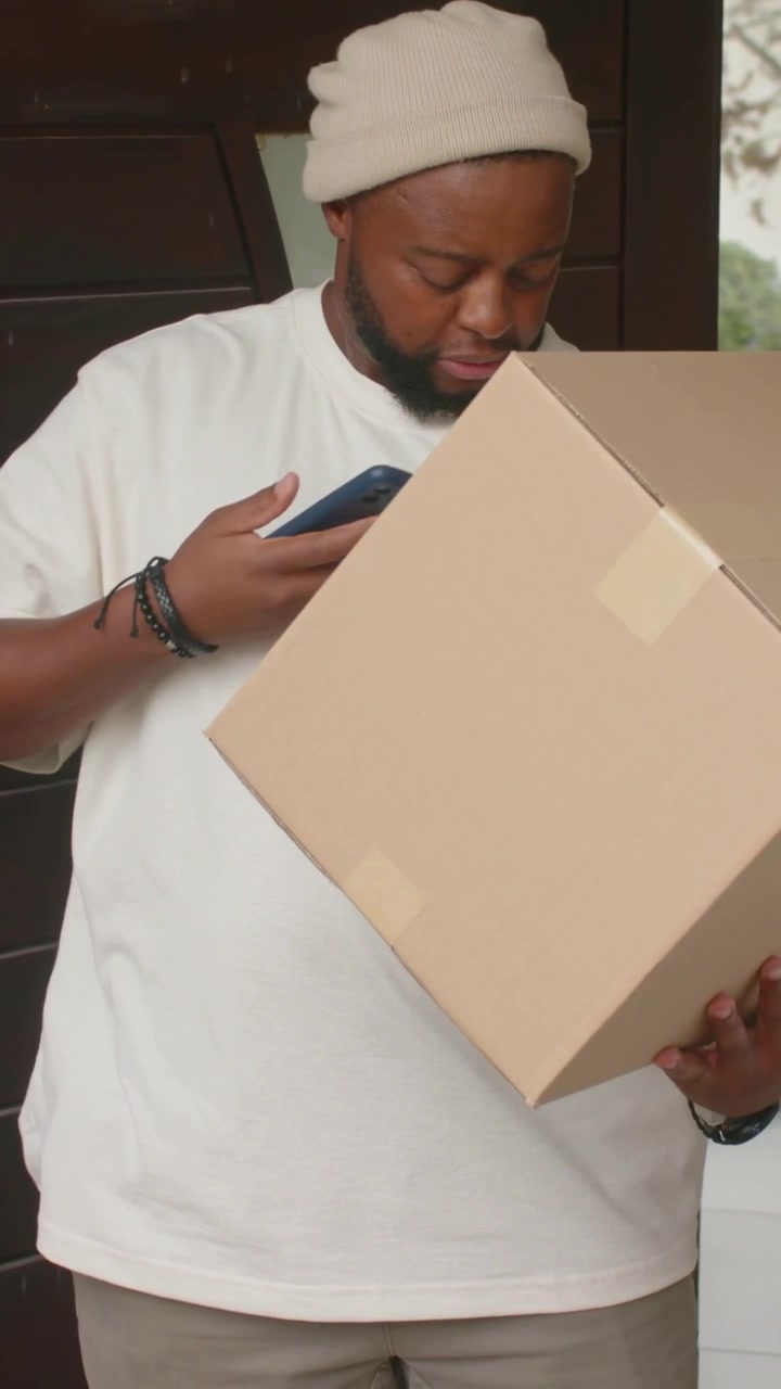 Vertical video: Phone buzzing, man in beanie, white tee checking phone, confirming package at door