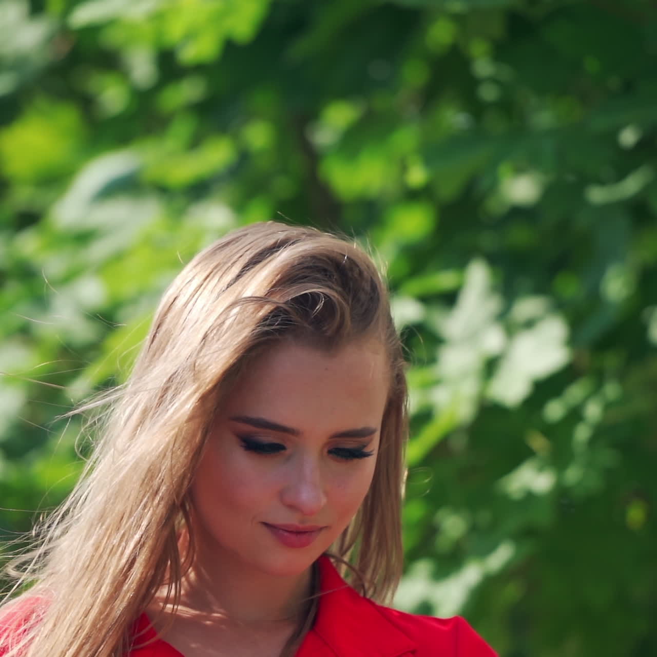 Beautiful woman doing selfie. Gorgeous young female in red dress photographing herself on the mobile phone outdoors.