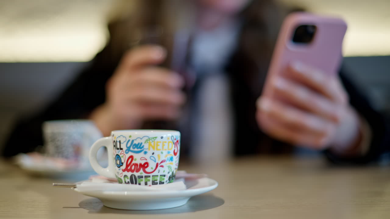 A cup of coffee at a cafe with a woman scrolling on her phone on the background