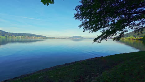 a calm blue lake widely surrounded by mountains and green trees on a sunny weather