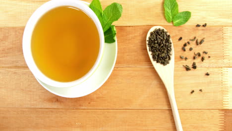 Close-up-of-tea-cup,-mint-leaves,-wooden-spoon,-dry-tea-leaves