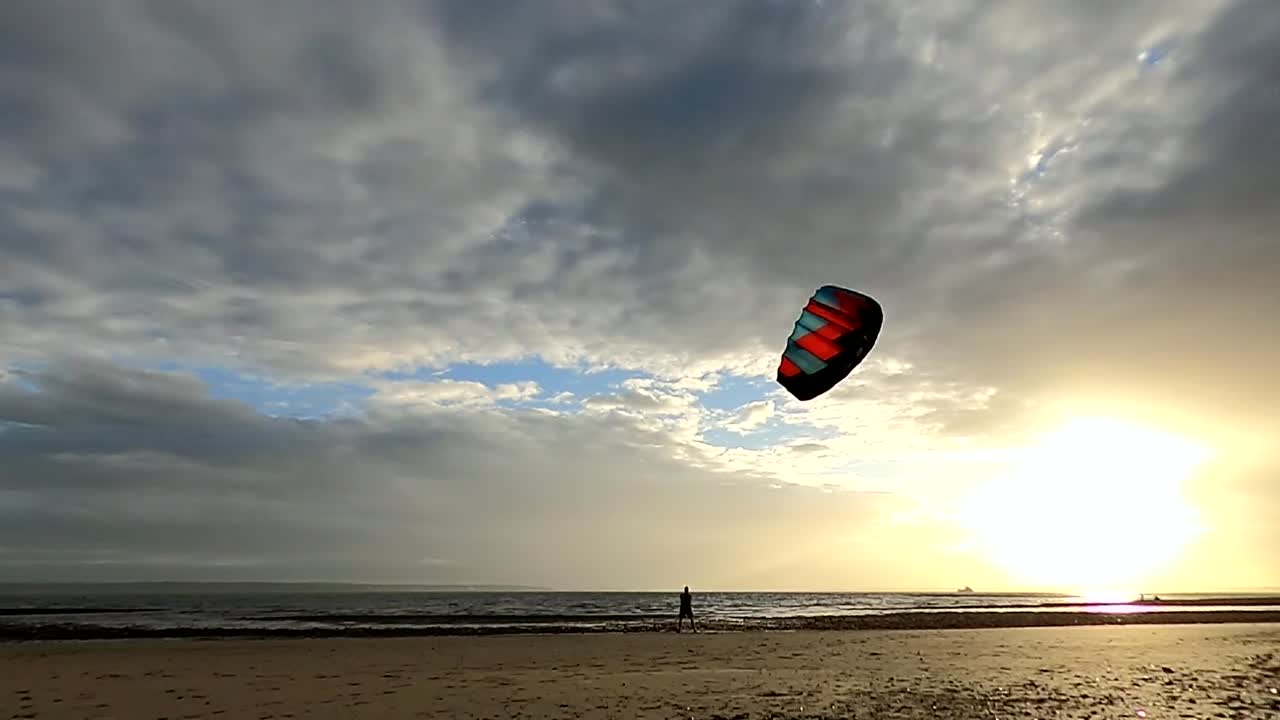 un hombre volando una cometa de poder rápidamente por el aire en cifras de 8 en una playa durante la puesta de sol
