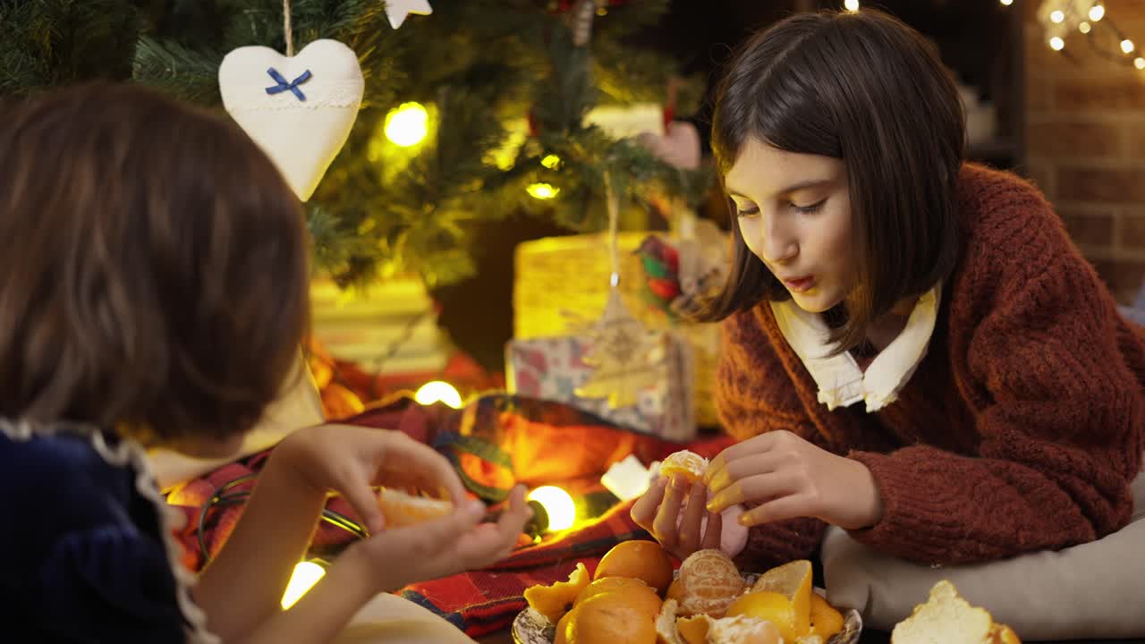 dos niñas tomando mandarinas bajo el árbol de navidad en las luces