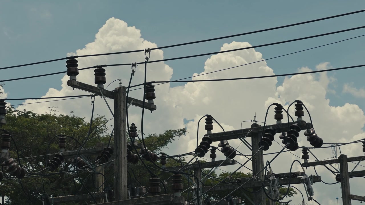 Detailed close up of an electricity pole top featuring primary distribution wires, insulators and utility components against a clear blue sky in an energy infrastructure setting.