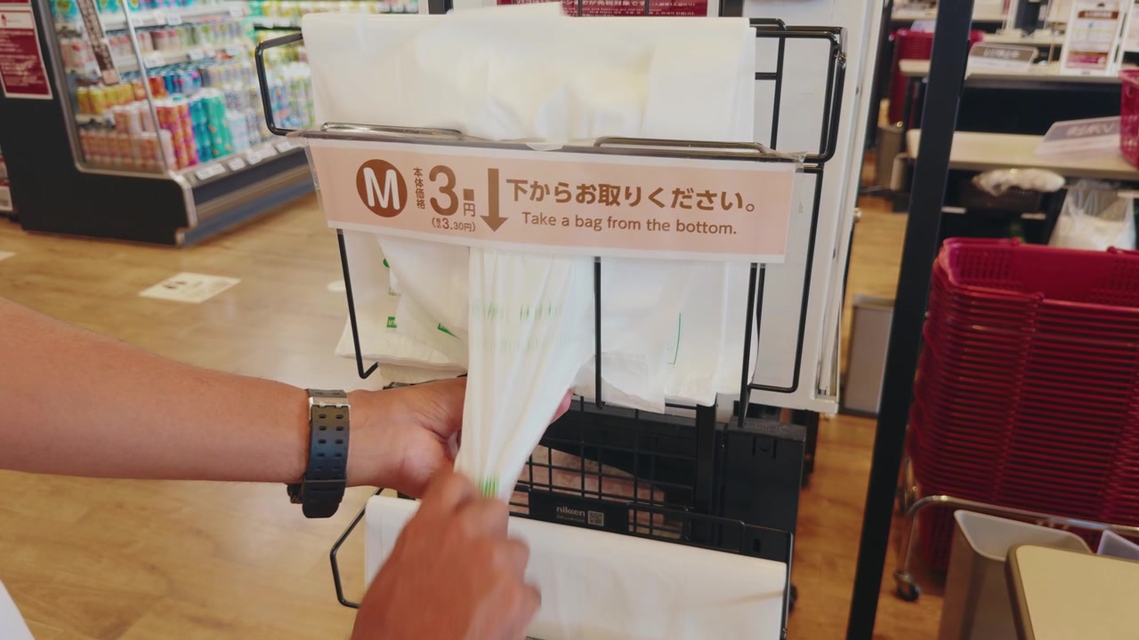 Japonya'daki bir süpermarkette kendi kendine hizmet veren bir dağıtıcıdan plastik poşet alan müşteri, günlük market alışverişini, perakende paketlemeyi ve ücretli poşet kullanımını gösteriyor