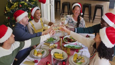 Happy-group-of-diverse-friends-in-santa-hats-celebrating-meal,-toasting-with-vine-at-christmas-time